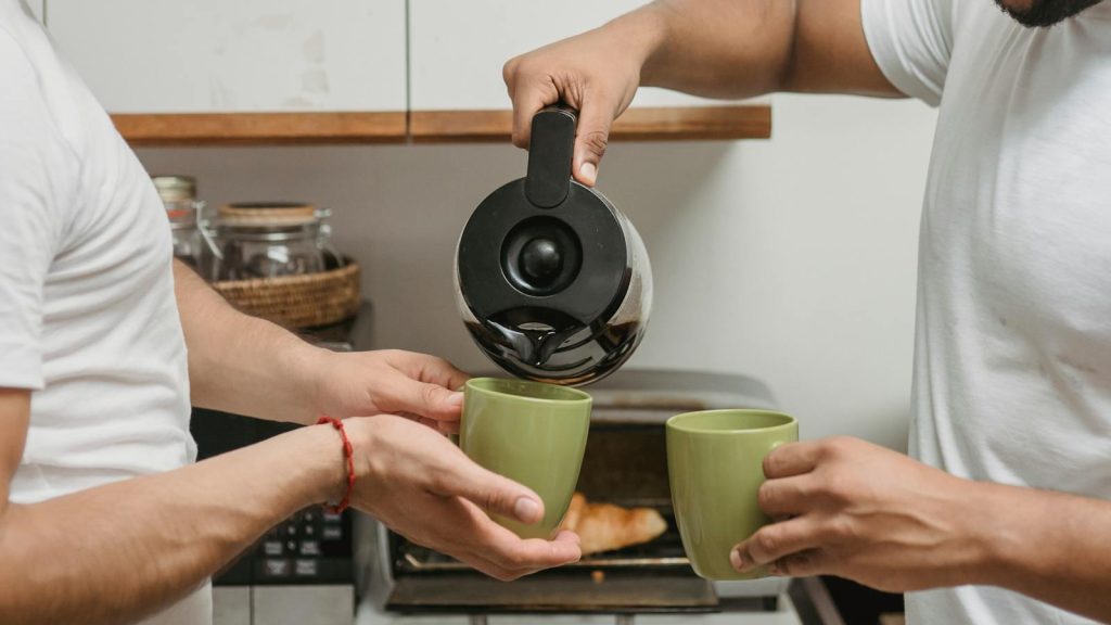 Two adults sharing a warm moment pouring coffee in a cozy kitchen.