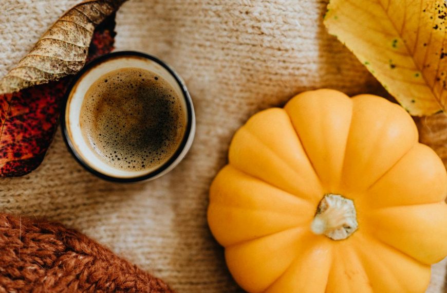 A warm autumn scene featuring coffee, a pumpkin, and fall leaves on a knitted blanket.