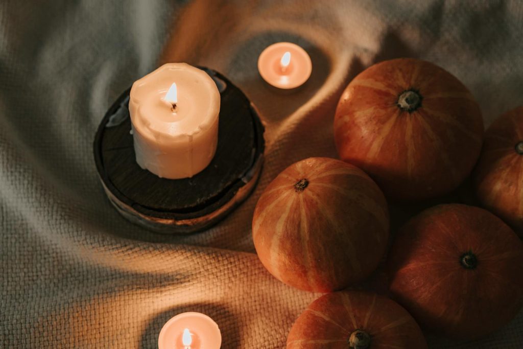 A warm autumn scene featuring lit candles and pumpkins on a cozy fabric.