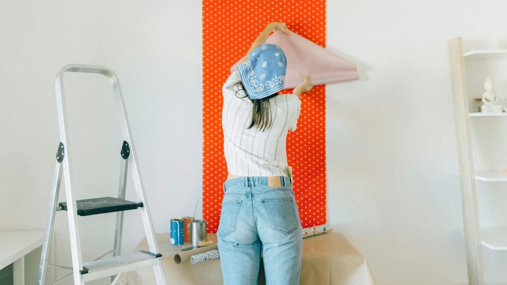 A woman applies polka dot wallpaper during a home makeover, showcasing DIY renovation.