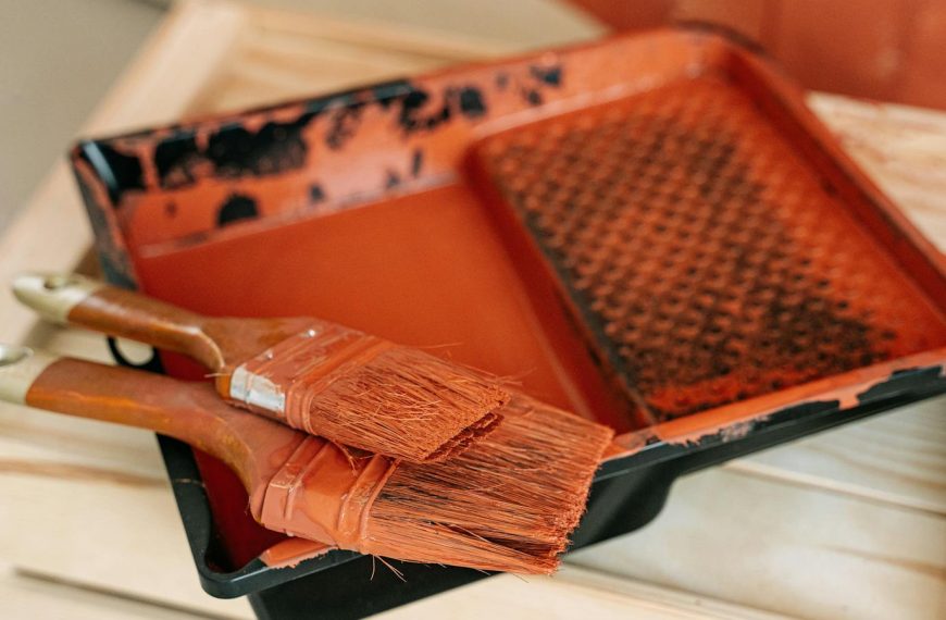 Paintbrushes resting on an orange paint tray during a painting project, indoors.