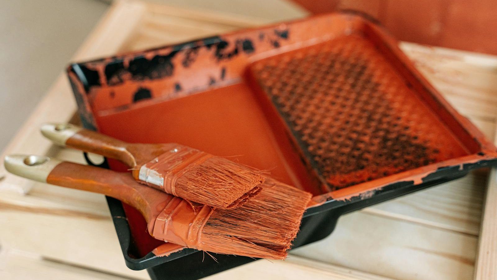Paintbrushes resting on an orange paint tray during a painting project, indoors.