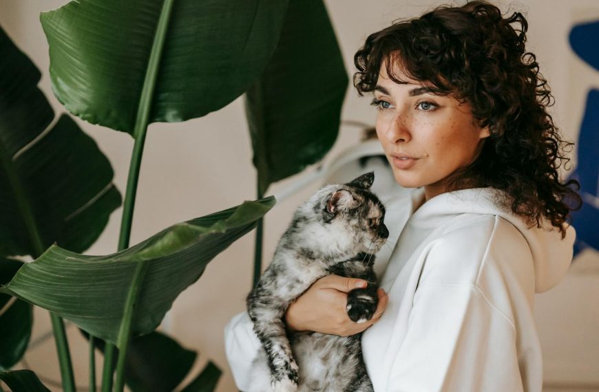 Serene moment of a woman holding her pet cat indoors surrounded by lush greenery.