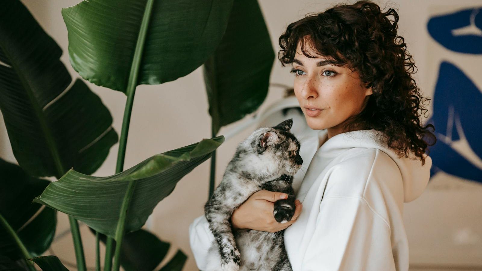 Serene moment of a woman holding her pet cat indoors surrounded by lush greenery.