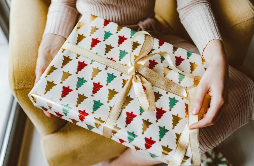 Woman holding beautifully wrapped Christmas gift with ribbon, creating a warm holiday ambiance.