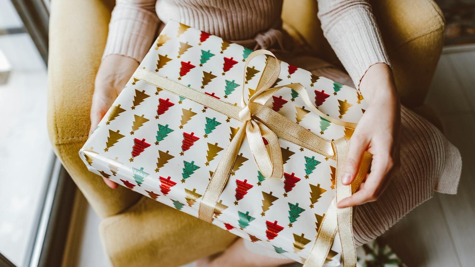 Woman holding beautifully wrapped Christmas gift with ribbon, creating a warm holiday ambiance.