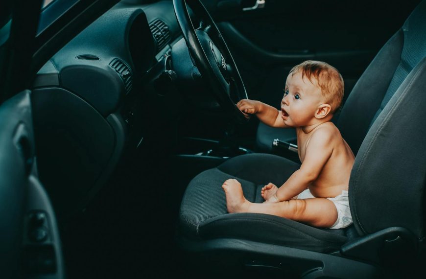 Cute baby sitting on the driver's seat of a car, looking curious and playful.
