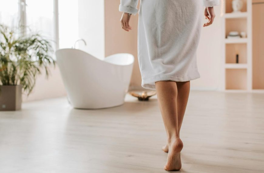 A person in a bathrobe walks towards a stylish bathtub in a bright, modern bathroom.