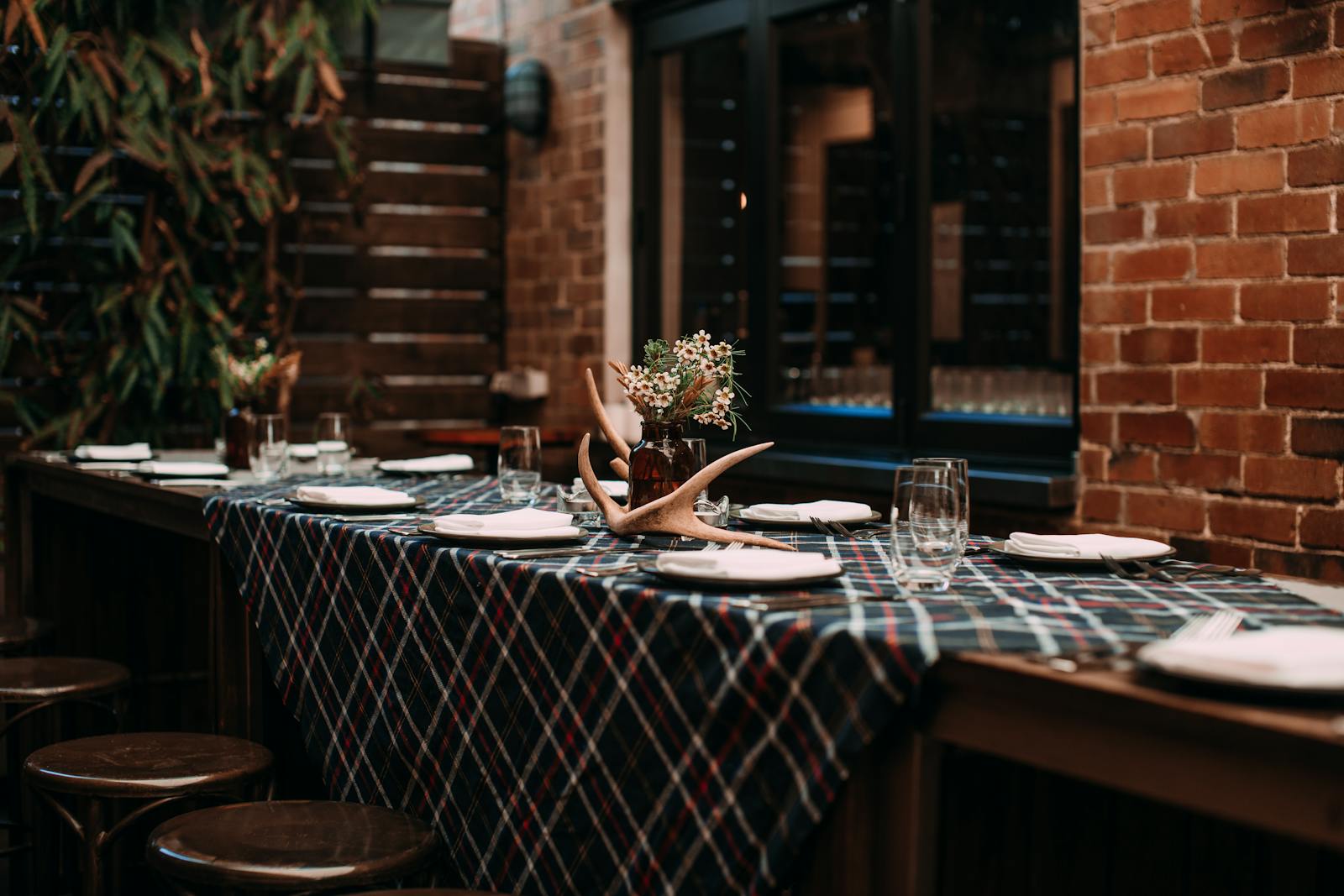 Elegant table setting with plaid tablecloth and flowers in a rustic brick-walled room, ideal for dining concepts.