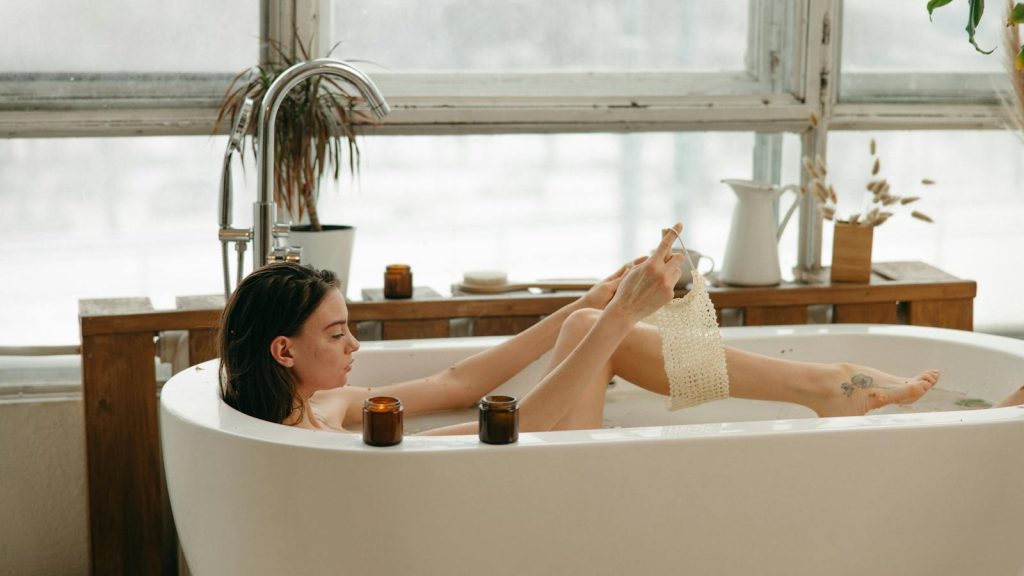 Woman in a bathtub with candles, relaxing and using a body scrub. Cozy indoor setting.