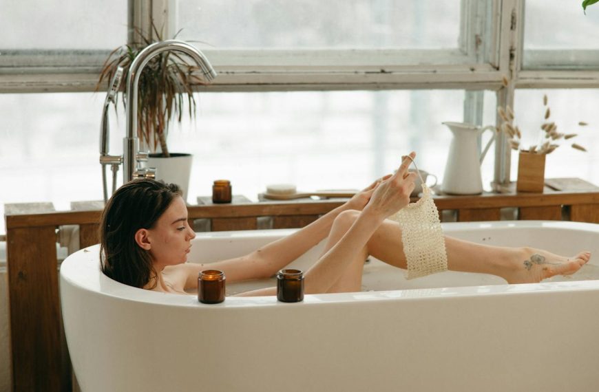 Woman in a bathtub with candles, relaxing and using a body scrub. Cozy indoor setting.