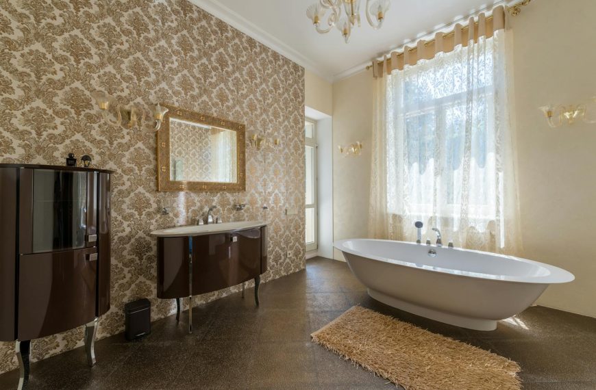 Luxury bathroom featuring a freestanding bathtub, ornate wallpaper, and ample natural light.