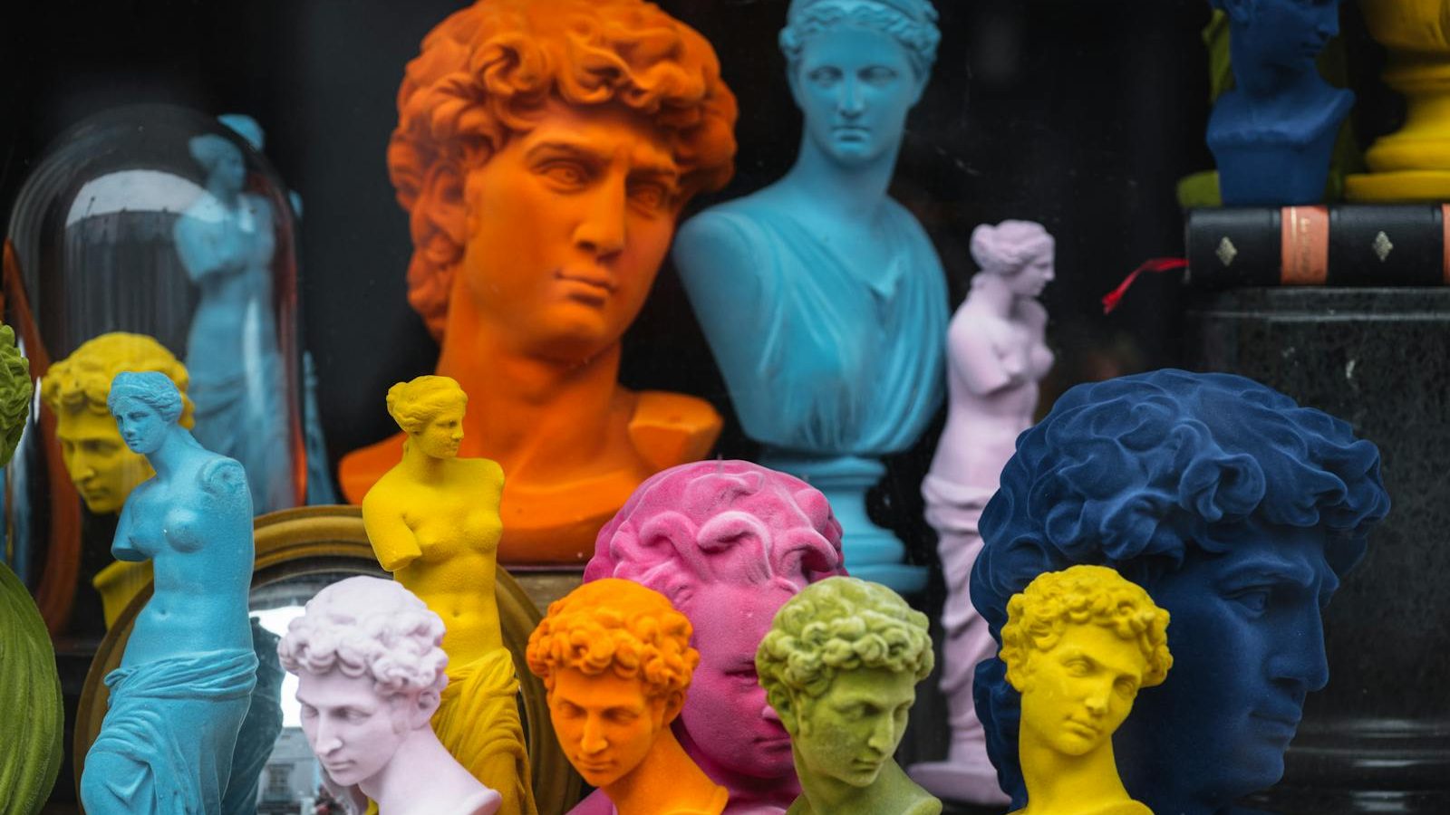 Multicolored head sculptures of David near bright statuettes placed in store with abundance of souvenirs and black pillar with book