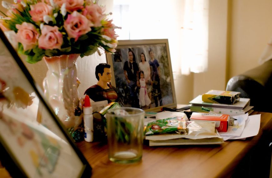 Frame with family photograph standing on wooden table among household items near bunch of flowers in daylight
