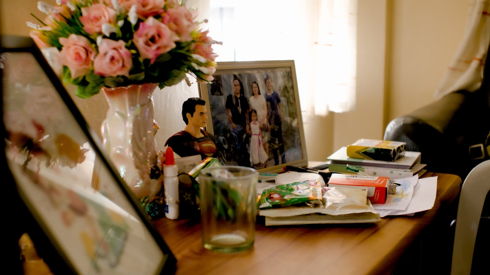 Frame with family photograph standing on wooden table among household items near bunch of flowers in daylight