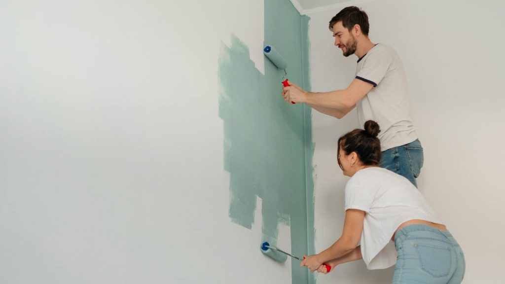 A young couple collaborates on painting a wall with rollers, highlighting teamwork and home improvement.