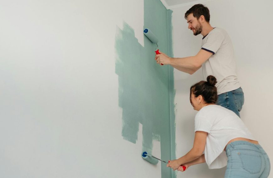 A young couple collaborates on painting a wall with rollers, highlighting teamwork and home improvement.