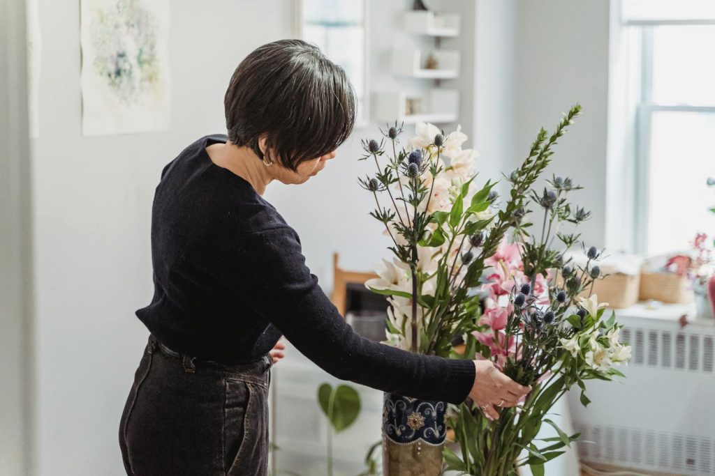 A woman carefully arranges a vibrant floral display in a well-lit home setting.