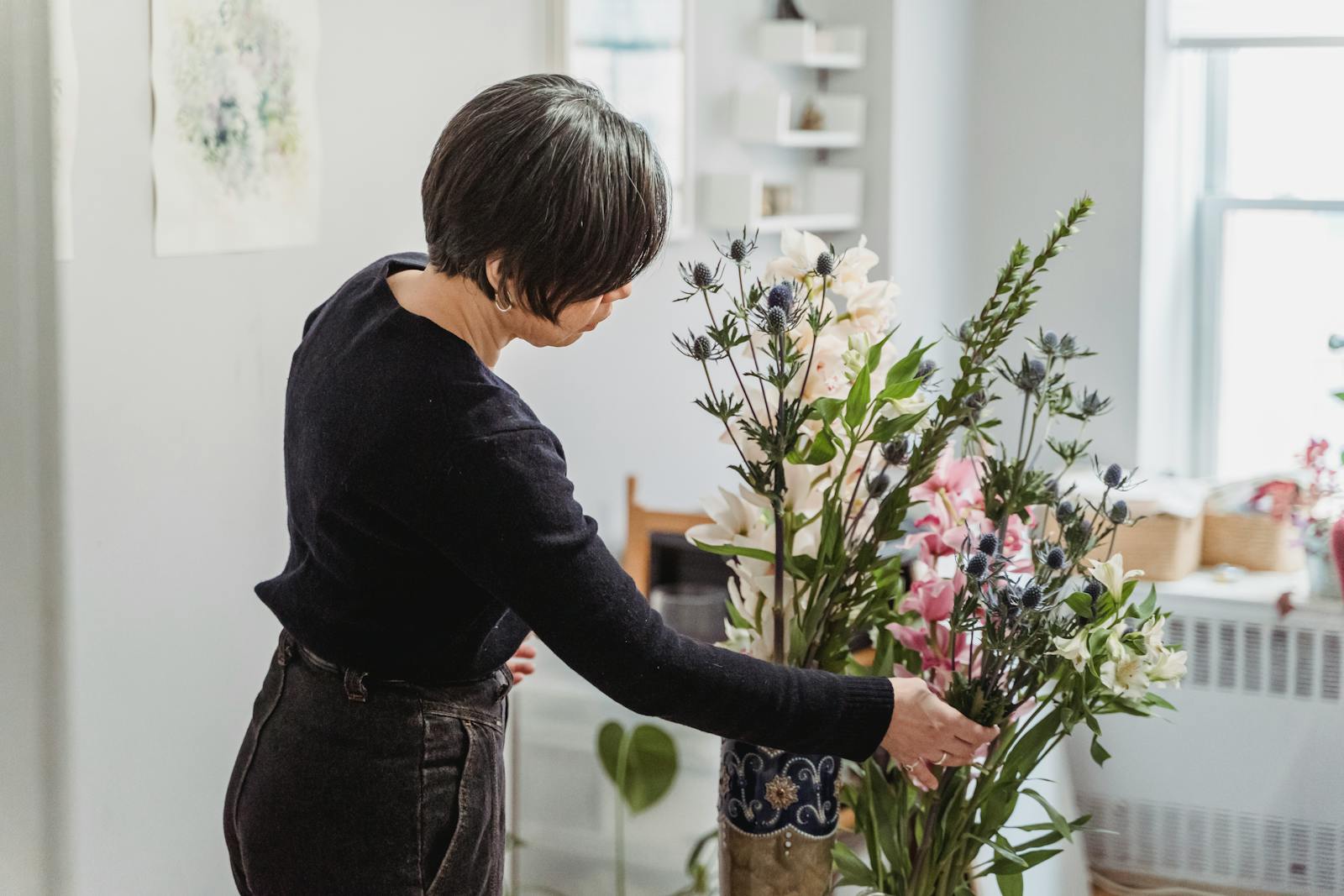 A woman carefully arranges a vibrant floral display in a well-lit home setting.