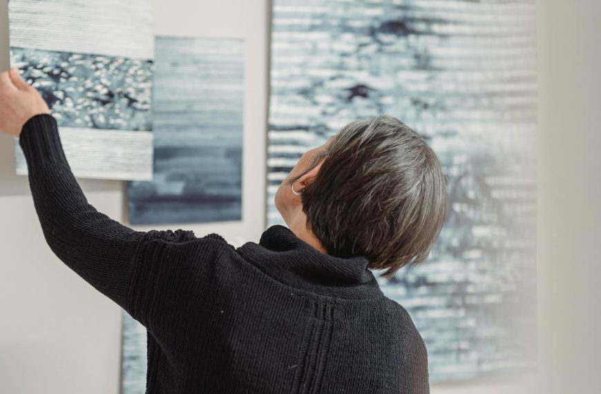 A woman arranges abstract art pieces on a gallery wall, showcasing modern creativity.