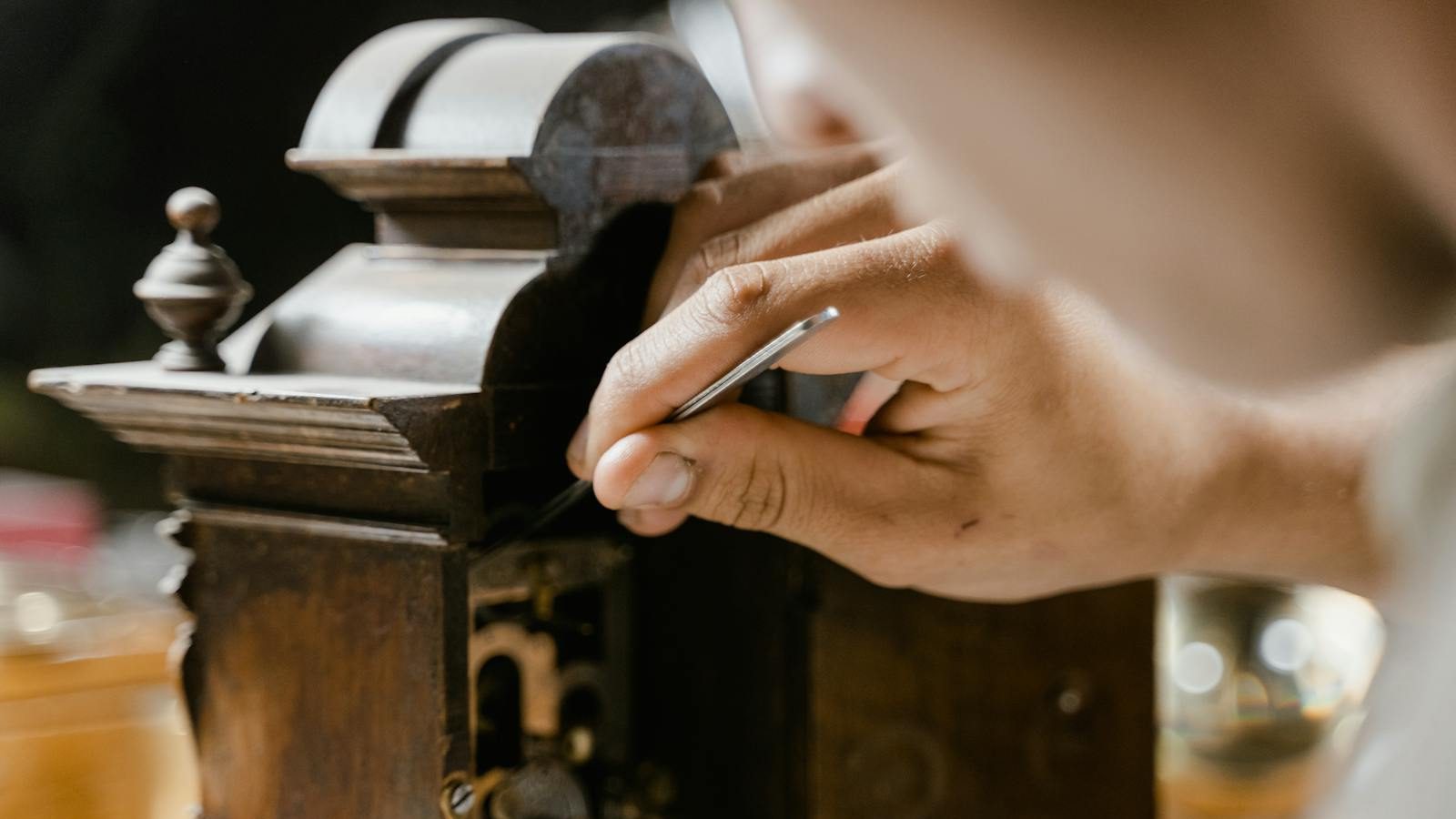 Close-up of hands skillfully restoring an antique wooden clock, highlighting craftsmanship.