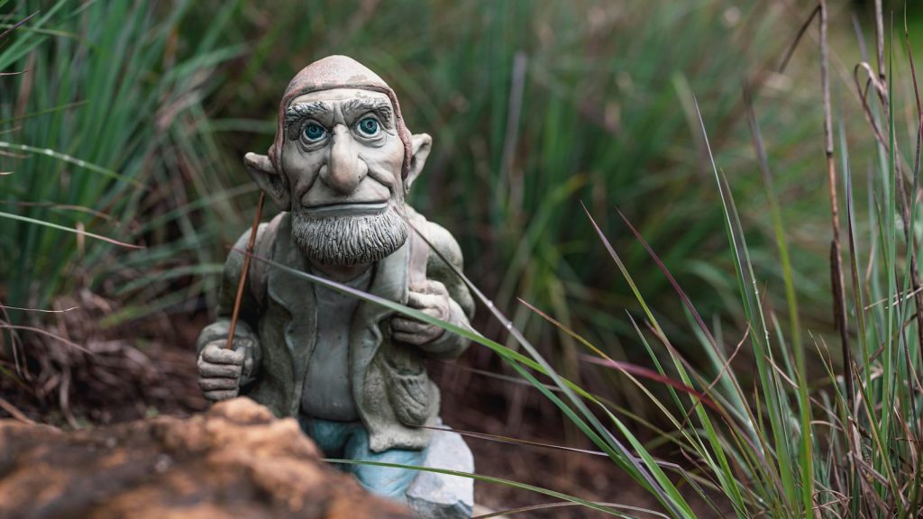 A charming garden gnome figurine sits nestled in vibrant grasses, adding whimsy to the outdoor space.