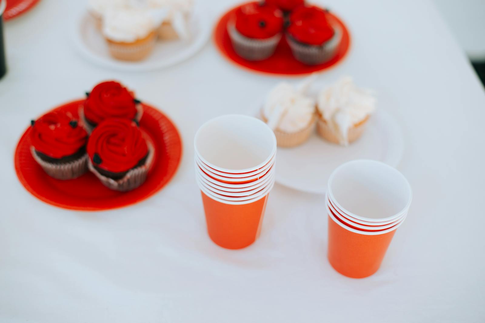 A vibrant table setup featuring red and white cupcakes with stacked orange disposable cups.