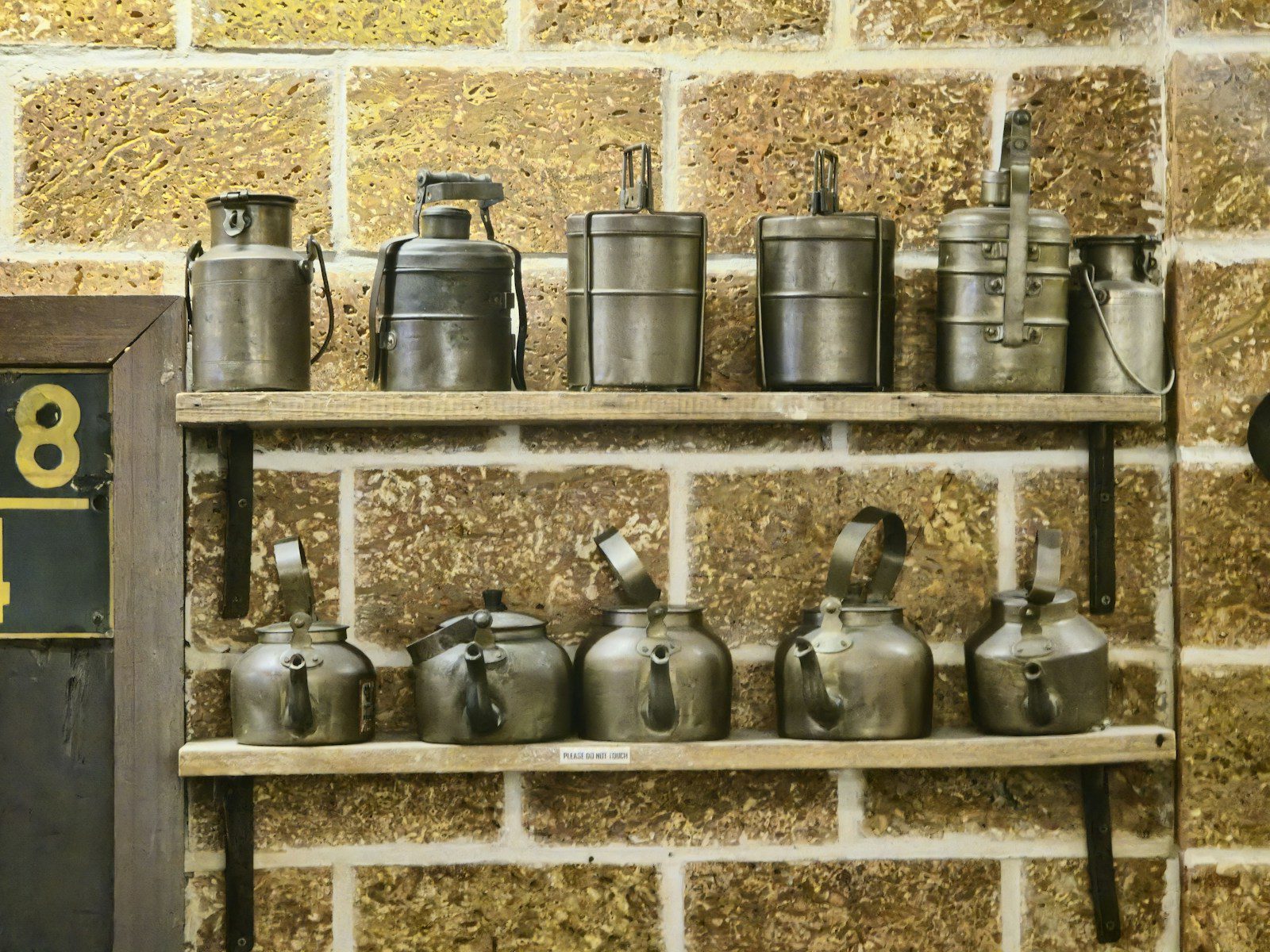 A shelf filled with pots and pans next to a brick wall