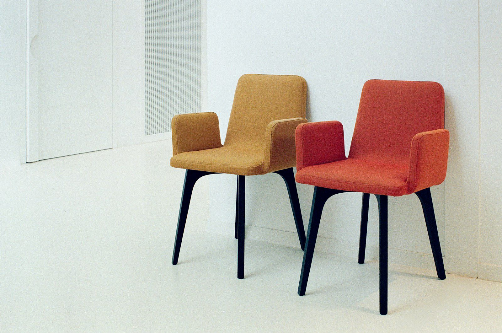 Two colorful chairs sit against a white wall.