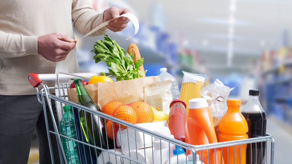 Man standing next to a full shopping cart and checking bill receipt cost