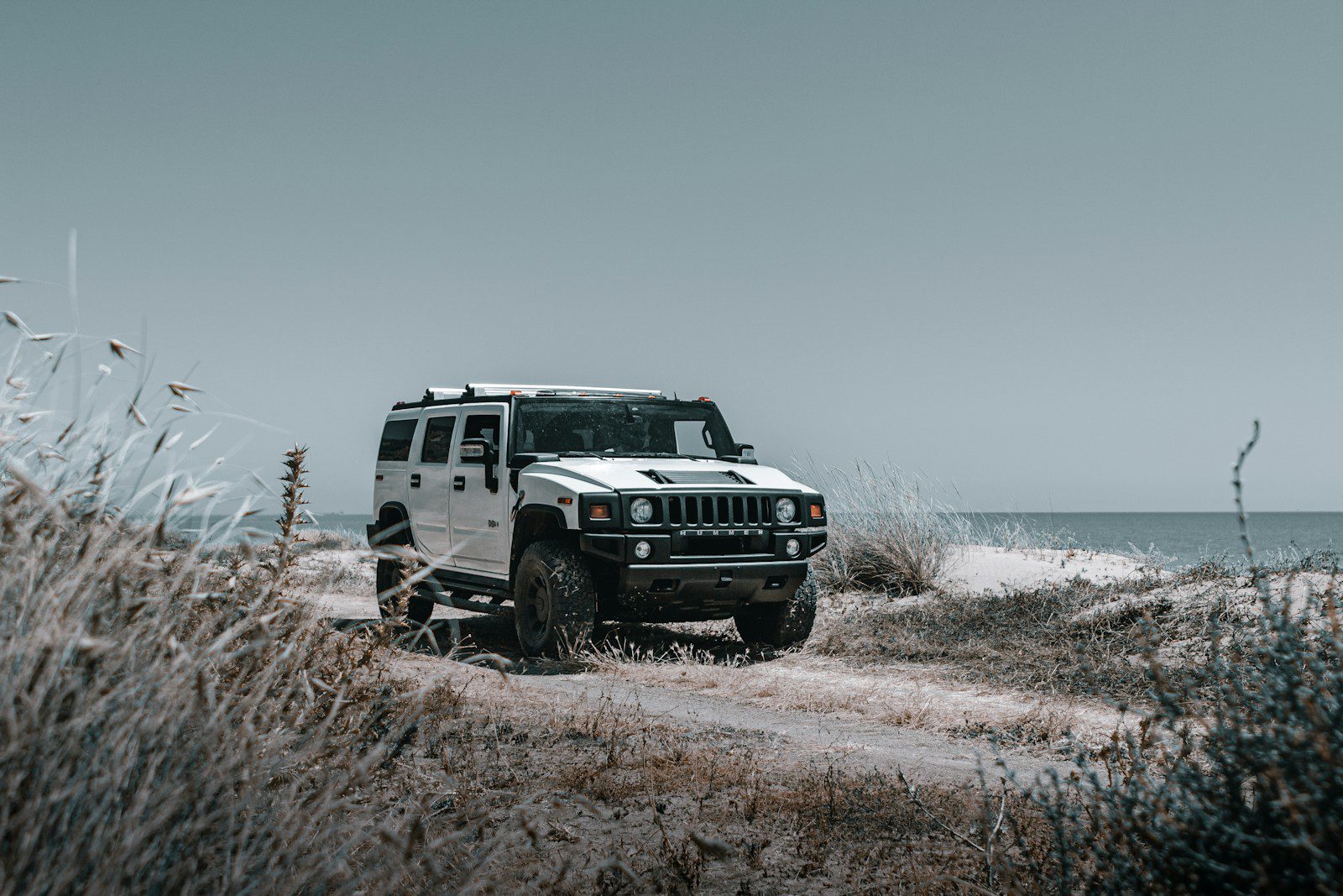 a white jeep driving down a dirt road next to the ocean