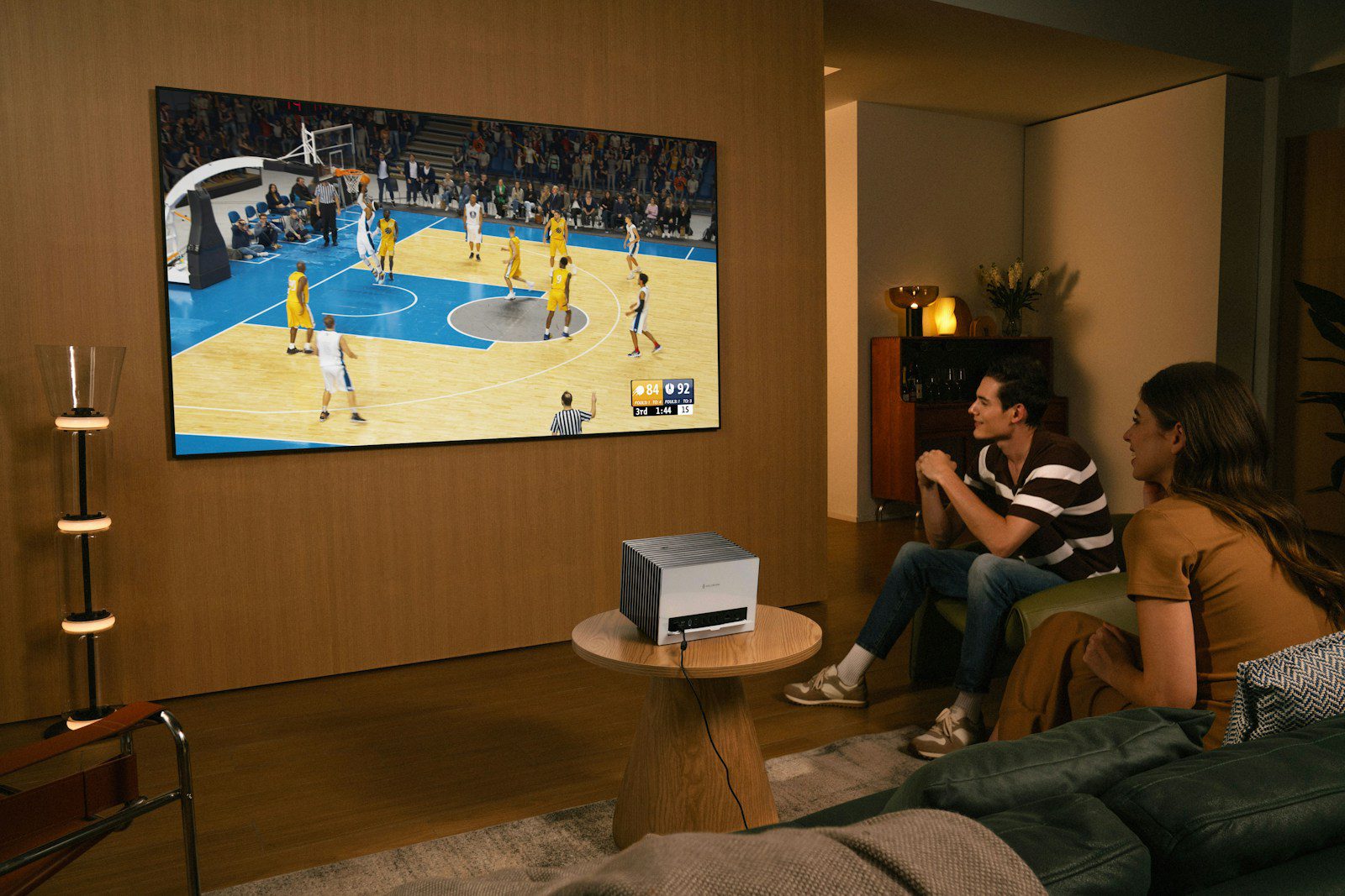 People watch a basketball game on a large screen.