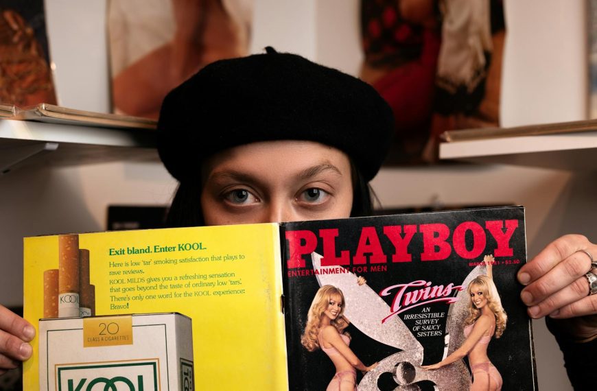 Woman in a black beret holding a vintage Playboy magazine with eyes peering over.