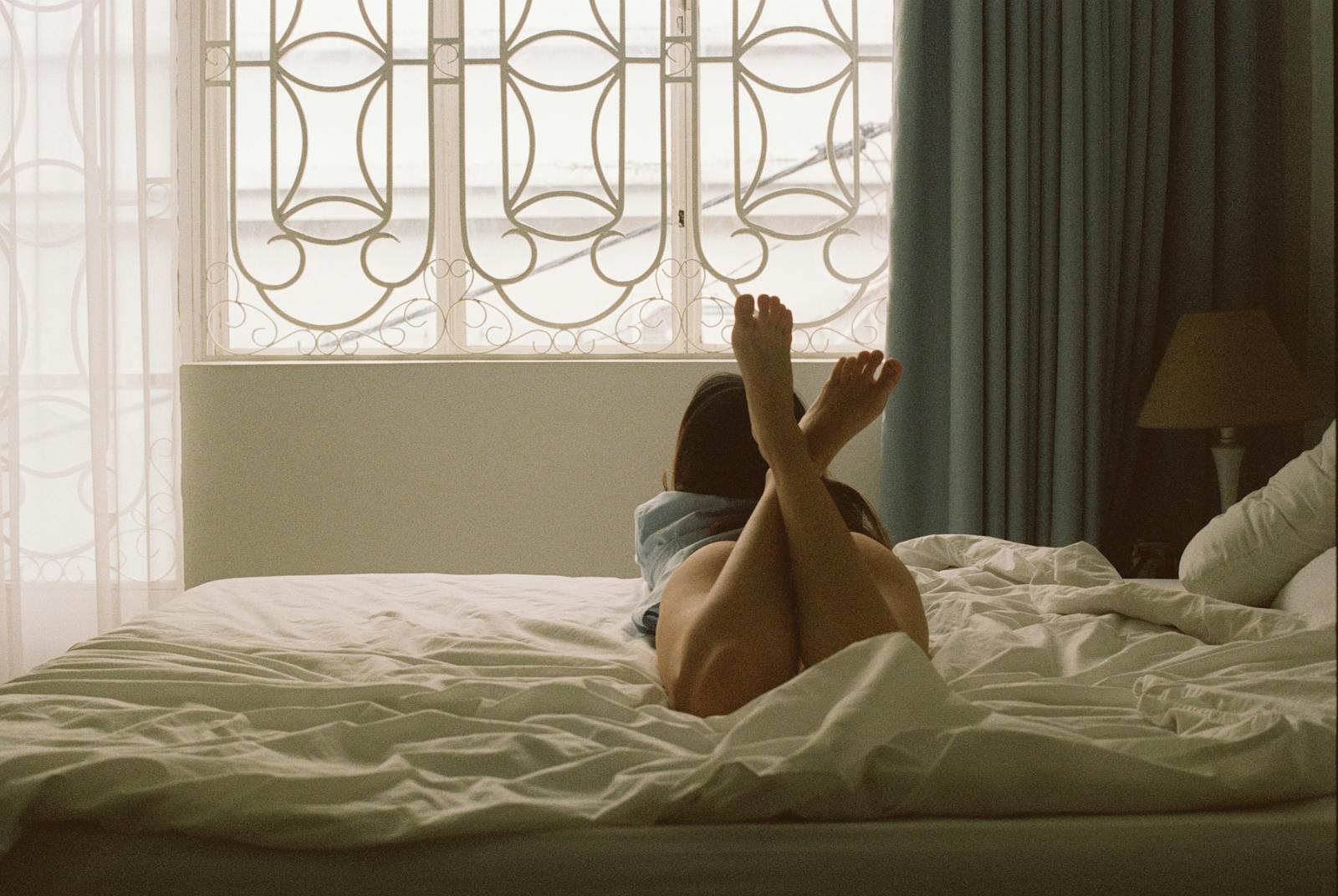 A woman relaxes on a bed with sunlight streaming through a modern bedroom window.