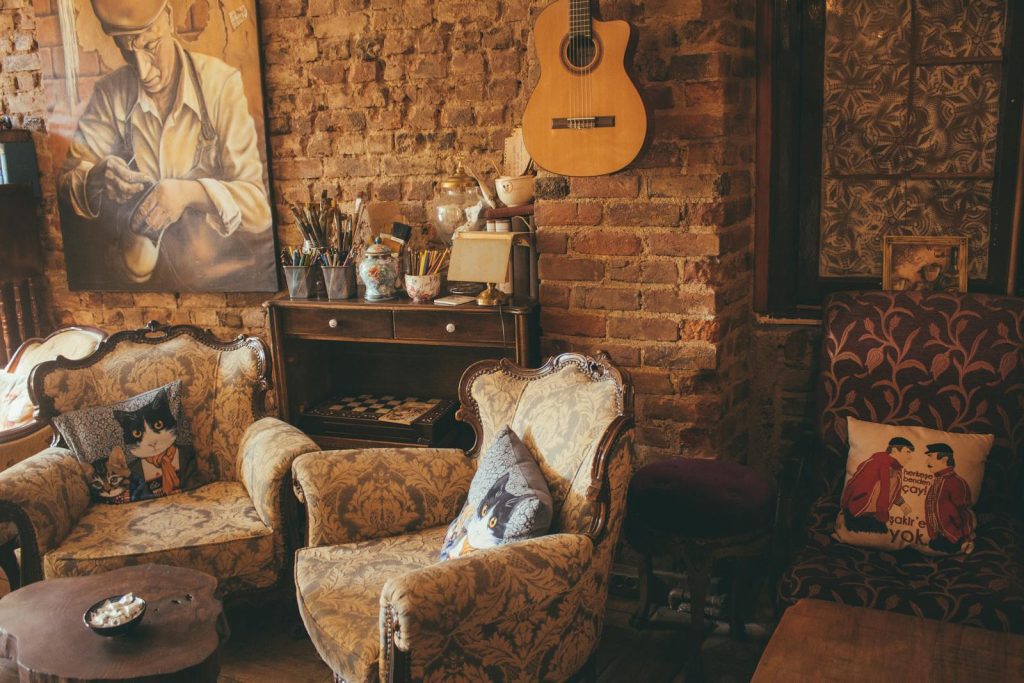 Warm vintage room with armchairs, guitar, and artwork on a brick wall, creating a cozy atmosphere.