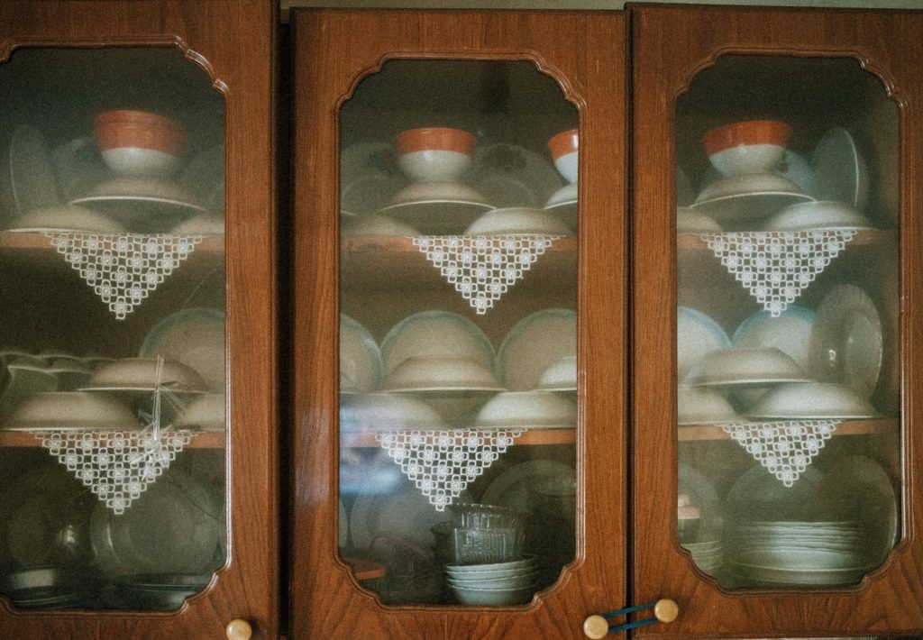 Vintage porcelain cups and plates elegantly displayed in wooden cabinets with lace decor.