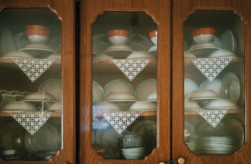 Vintage porcelain cups and plates elegantly displayed in wooden cabinets with lace decor.