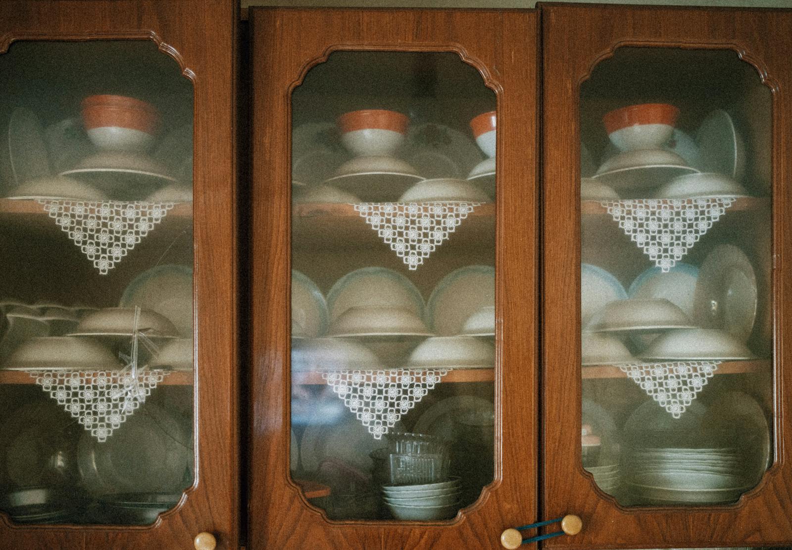 Vintage porcelain cups and plates elegantly displayed in wooden cabinets with lace decor.