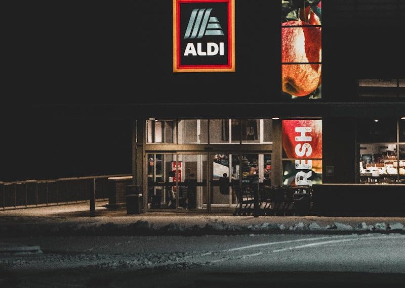 A nighttime winter view of an Aldi storefront with a prominent logo, captured in Roeland Park, KS.