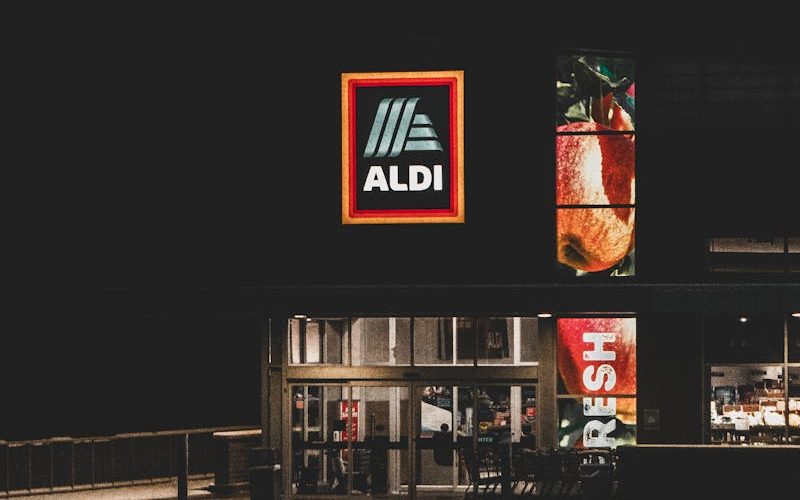A nighttime winter view of an Aldi storefront with a prominent logo, captured in Roeland Park, KS.
