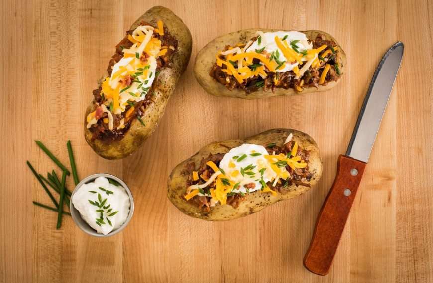 Mouth-watering loaded baked potatoes with cheese, sour cream, and chives on a wooden surface.