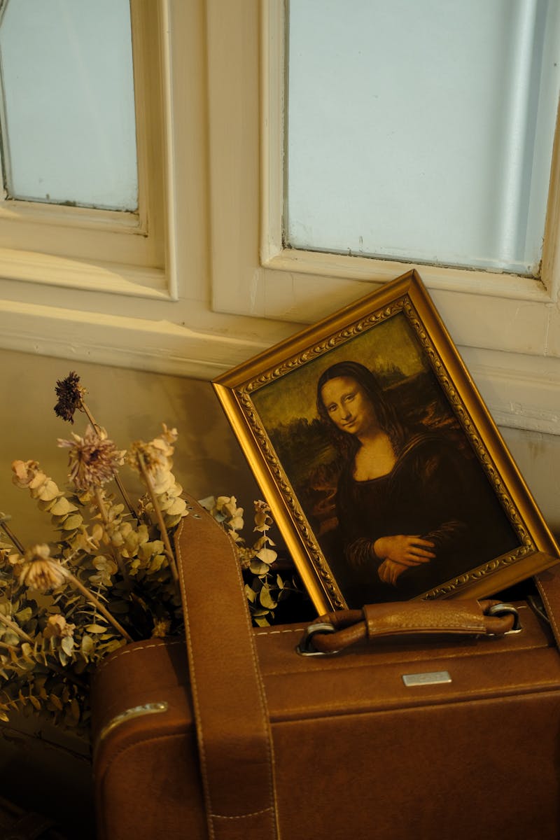 A vintage suitcase with a framed Mona Lisa print and dried flowers, evoking a nostalgic and artistic atmosphere.
