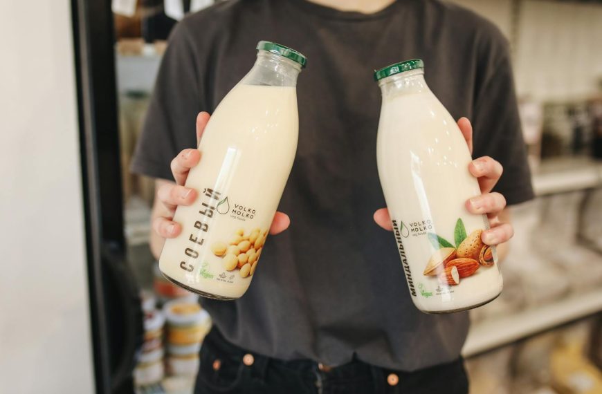 Person holding bottles of almond and soy milk substitutes in a store.