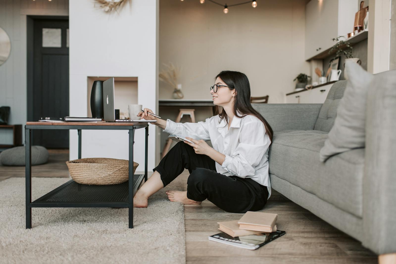 Woman using a laptop while sitting on the floor of a cozy living room, epitomizing work-from-home lifestyle.