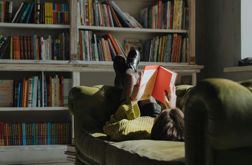 Young woman reading on a green sofa in a library, enjoying leisure time.