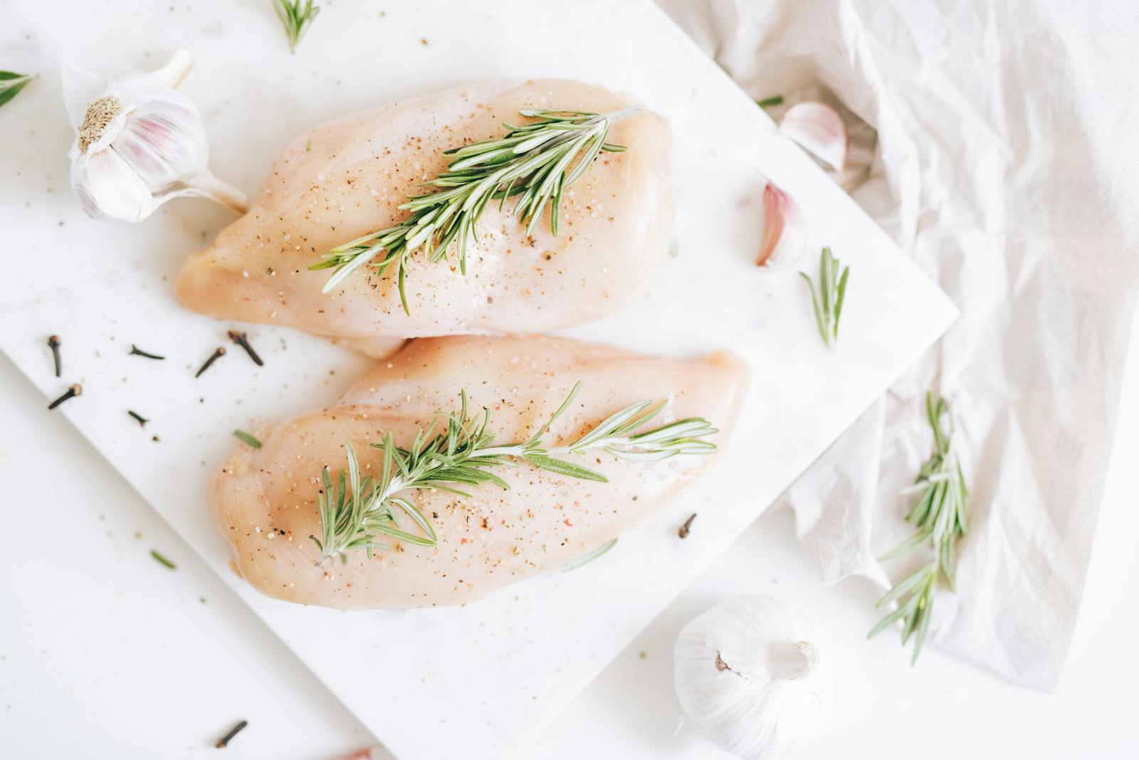 Raw chicken breasts seasoned with rosemary and garlic on a cutting board.
