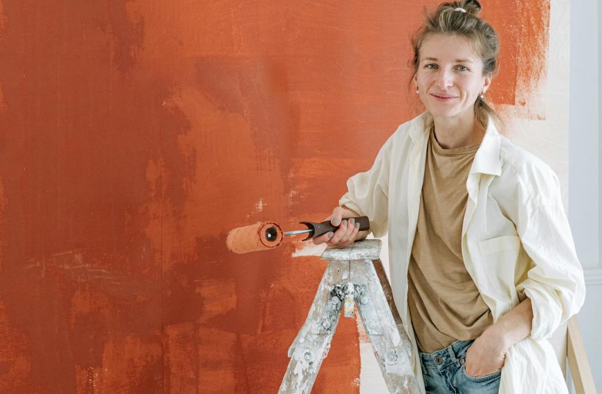 Woman smiling while painting a wall with a roller during a home renovation project.