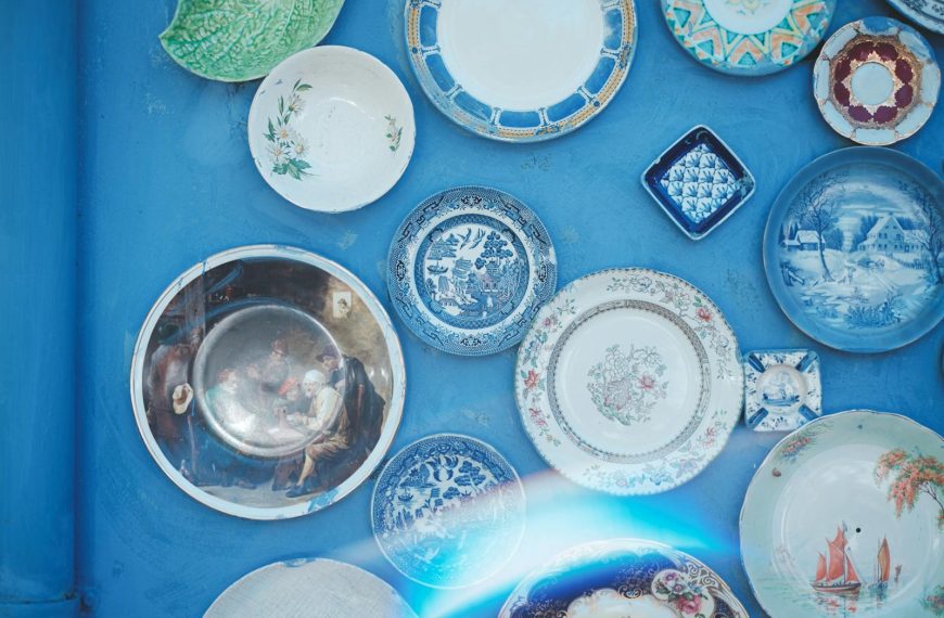 Assorted vintage plates of different sizes and ornaments hanging on bright blue wall in light studio