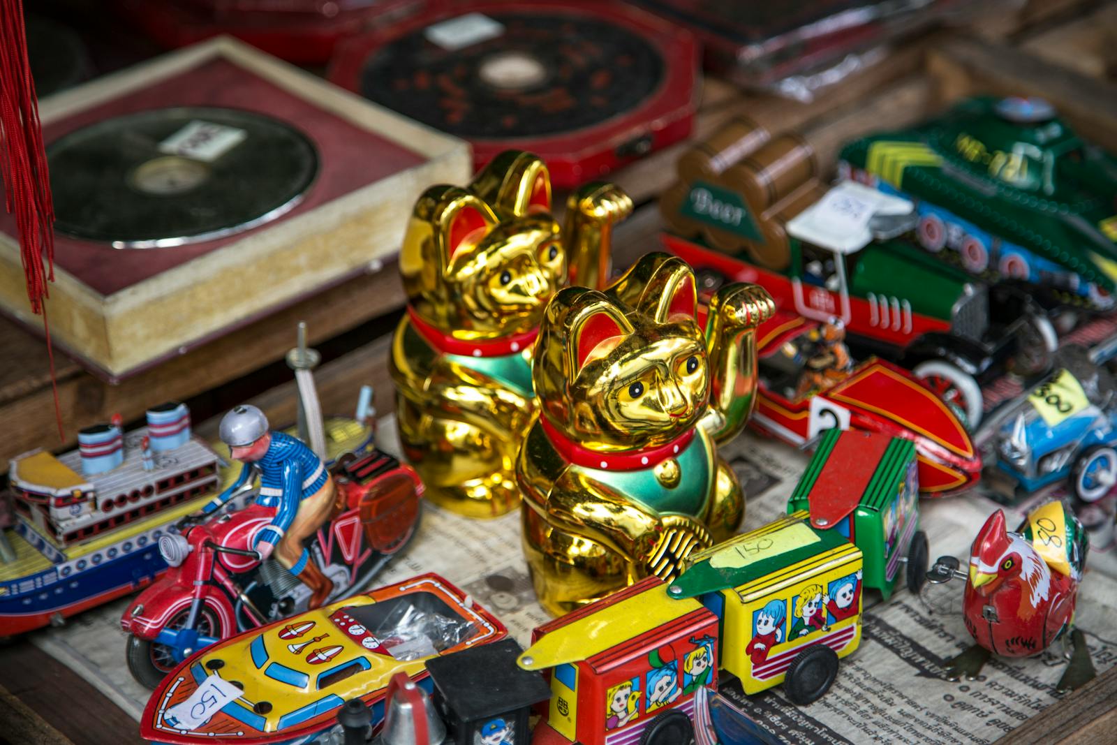 A vibrant display of vintage toys, featuring Maneki-neko figurines and tin vehicles, creating a retro feel.