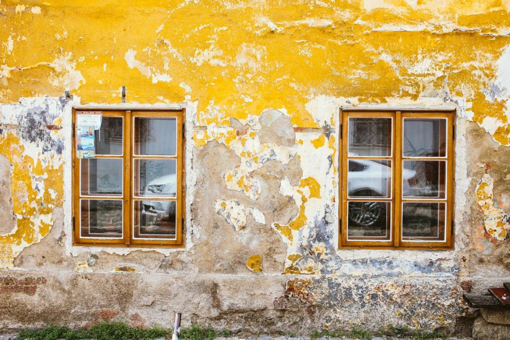 Old textured wall with rustic windows showcasing peeling paint and reflections.